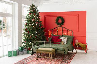 A christmas decorated bedroom with a christmas tree and a wreath on the wall. a double bed 