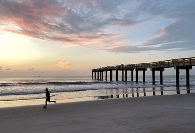 Silhouette person on beach against sky during sunset