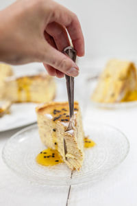 Cropped hand cutting dessert with fork on table