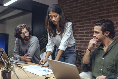 Businesswoman explaining business strategy on chart to colleagues with laptop in meeting at office