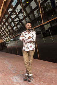 Bearded man with crossed arms while standing against office building.