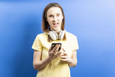 Portrait of smiling woman holding smart phone while standing against blue sky