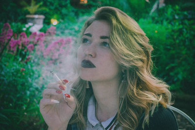 Young woman smoking cigarette while looking away against plants