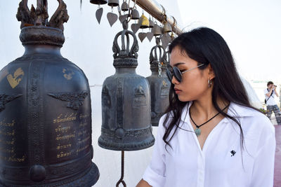 Close-up of young woman standing by bells against sky