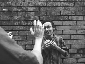 Cropped hands of man with male friend standing against brick wall