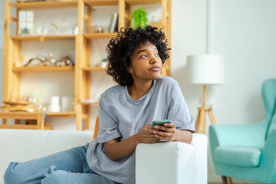 Young woman using mobile phone while sitting at home