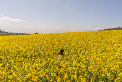 Scenic view of oilseed rape field against sky and a girl in the middle 