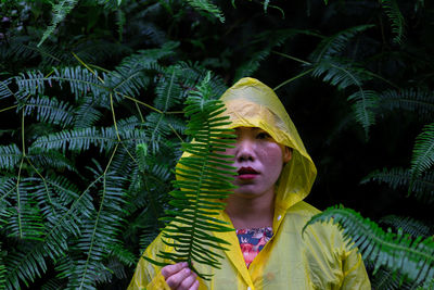 Portrait of woman wearing raincoat while standing amidst plants during rainy season