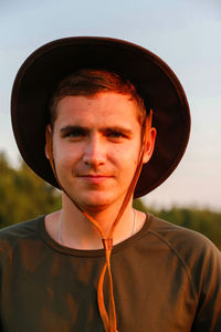 Young man smiling farmer in cowboy hat at agricultural field on sunset with sun flare. portrait 