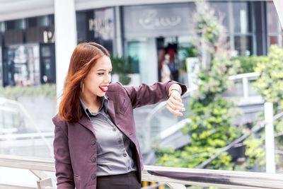 Smiling young businesswoman checking time while standing on elevated walkway 