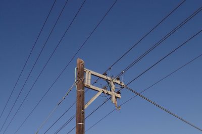 Low angle view of electricity pylon against clear blue sky