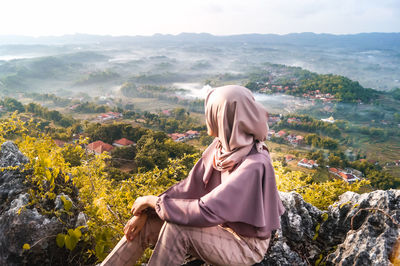 Side view of man sitting on plants against mountain