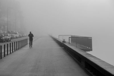 Rear view of man walking on bridge in foggy weather