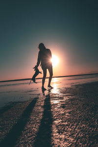 Silhouette people on beach against sky during sunset