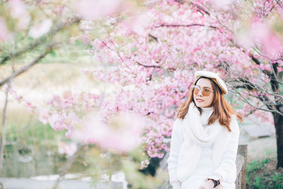 Beautiful woman standing by pink flowering tree