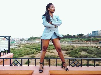 Full length portrait of young woman standing against railing