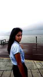 Young woman standing on promenade against cloudy sky