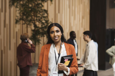 Portrait of smiling female entrepreneur holding diary while standing at convention center