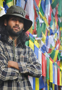 A young guy looking at camera posing with his arms crossed, standing against buddhist prayer flags