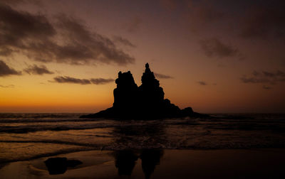 Silhouette rock on beach against sky during sunset