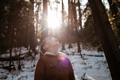 Young boy in forest looking up at the sun in the winter