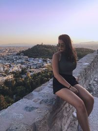 Woman sitting on stone wall in city