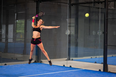 Woman playing padel in a blue grass padel court indoor - sporty woman padel player hitting ball 