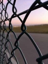 Close-up of chainlink fence against sky during sunset