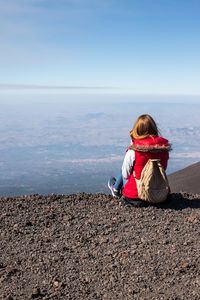 Rear view of woman sitting on rock against sky