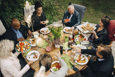 High angle view of senior male and female friends enjoying dinner at dining table during back yard garden party