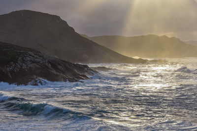 Big waves break on the coast, in the sunlit sea, passing through the clouds sunset. galicia, spain.
