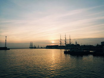 Silhouette of factory by sea against sky during sunset