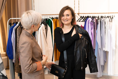 Young women choosing clothes at store, sales consultant offers wear