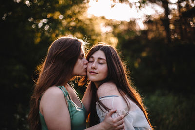 Young woman kissing her girlfriend on the cheek in forest in summer