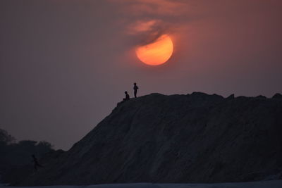 Silhouette people standing on rock against sky during sunset