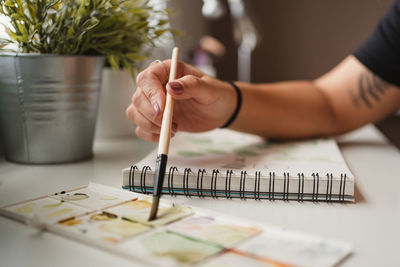 Closeup of unrecognizable woman using palette and watercolors while creating picture and sitting at table at home in paris