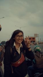 Portrait of smiling young woman gesturing peace sign against sky