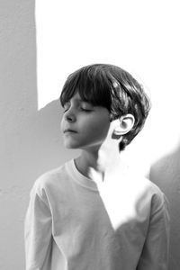 Boy with eyes closed standing against wall