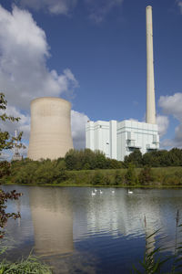 View of factory by lake against sky