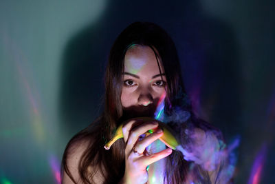 Close-up portrait of woman holding banana in darkroom