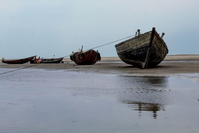 Abandoned boat moored on beach against sky