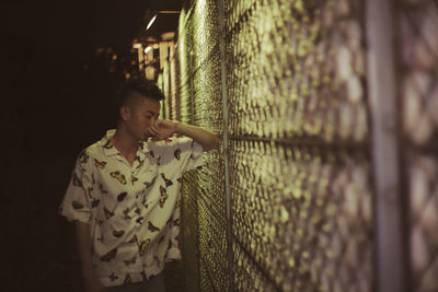 Young man looking while standing by chainlink fence
