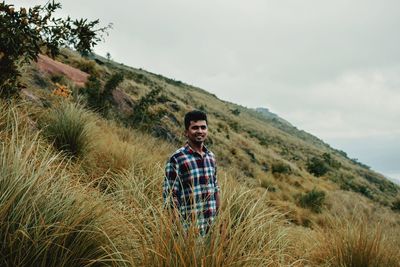 Portrait of young man standing by plants against sky