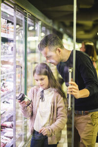 Daughter holding bottle by father at refrigerator in supermarket