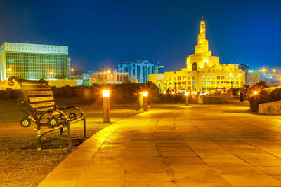 Illuminated street amidst buildings against sky at night