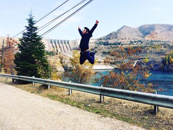 Young man jumping in mid-air with river and mountain in background