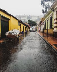 Wet street amidst buildings in city