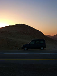 Car on desert against sky during sunset