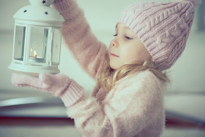 Close-up of cute girl wearing warm clothing holding oil lamp at home