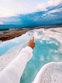 Cropped hand of woman holding sand at beach against sky, pamukkale